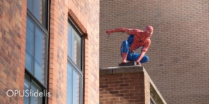 Spider-Man crouches on the edge of a brick building.