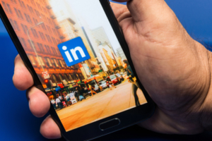 Miami, Florida, USA- May 27, 2013: Linkedin, Man hand holding a samsung note II smart phone showing the Linkedin application web page on blue background. Linkedin is a business oriented social networking site where is it possible to show own skills and contacts.